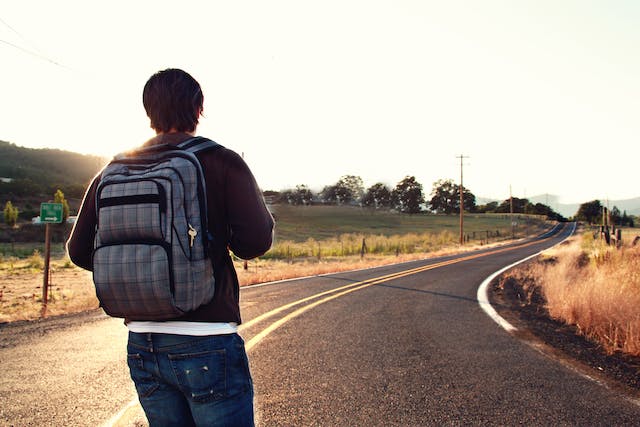 Rapaz de costas andando em uma estrada com uma mochila nas costas depois da autorização de viagem.