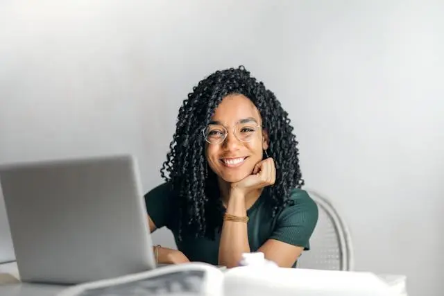 Mulher negra, de óculos e cabelos cacheados sorrindo com um notebook à sua frente para o reconhecimento de firma digital no cartório.