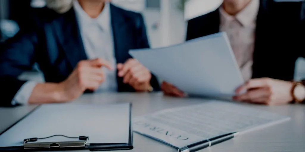 Duas pessoas sentadas em uma mesa com documentos para fazer o apostilamento.